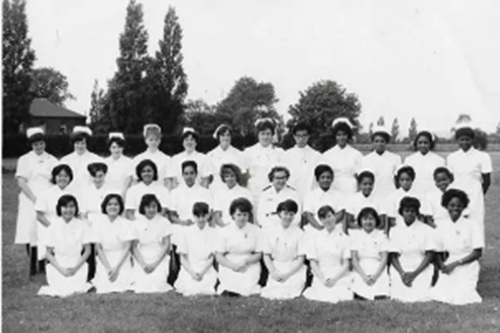 A black and white photo of nurses in uniform posing in rows on a field, smiling at the camera.